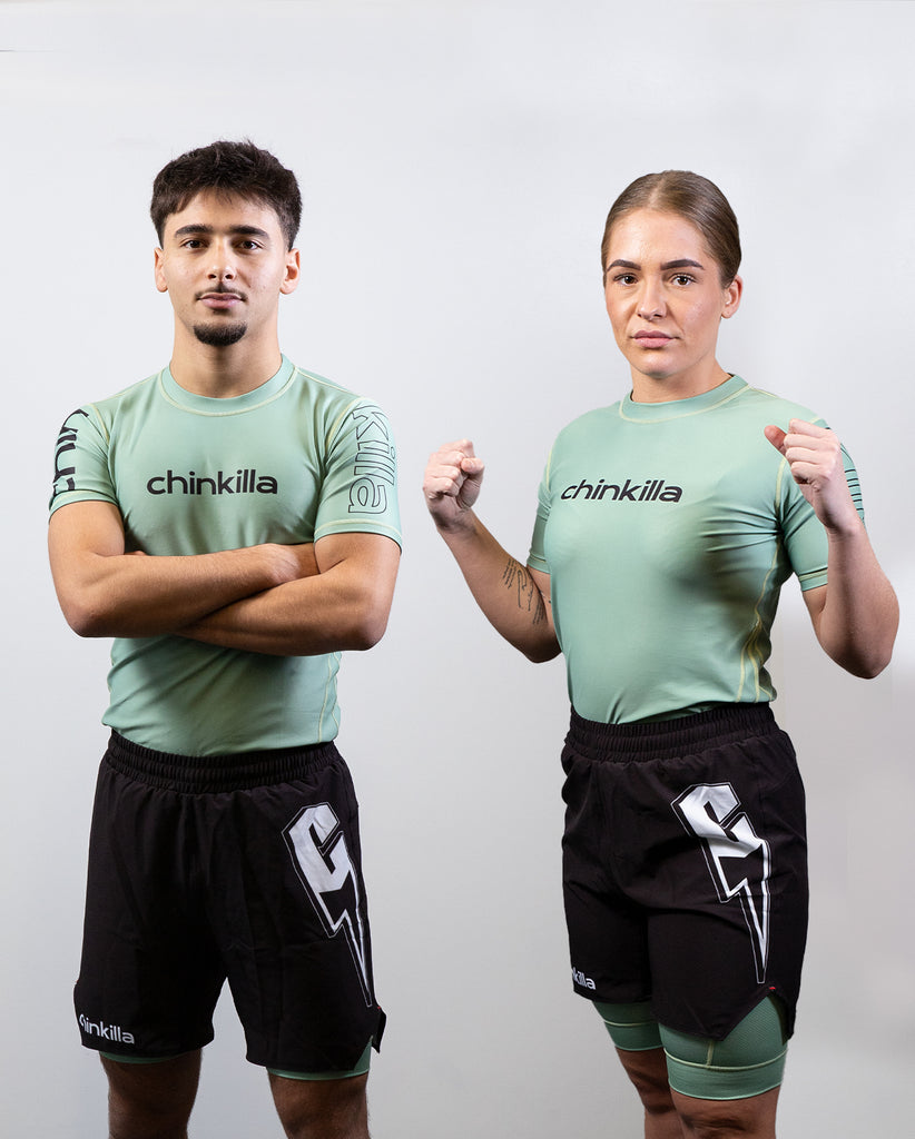 man and woman wearing a unisex chinkilla fight set - green rashguard and black shorts with green undershort